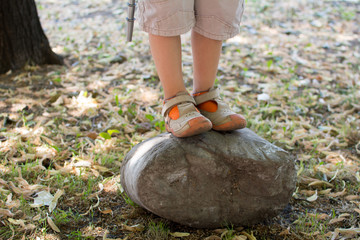 Child legs. Kid is standing on a rock in park. Focus on left shoe, when viewed from the front.