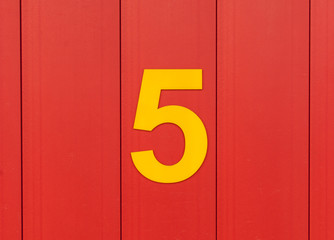 the number five, yellow, set against bright red wood