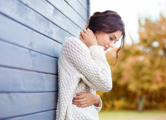 Beautiful natural young brunette woman wearing knitted sweater by the house. Fall and winter fashion concept.