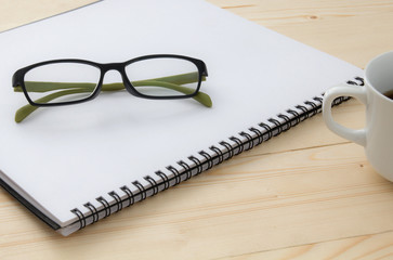 glasses on notebook and a cup of coffee on wood table