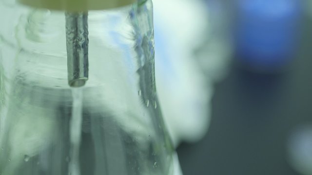 Panning shot of liquid falling in flask at laboratory. Solution being prepared for scientific experiment.
