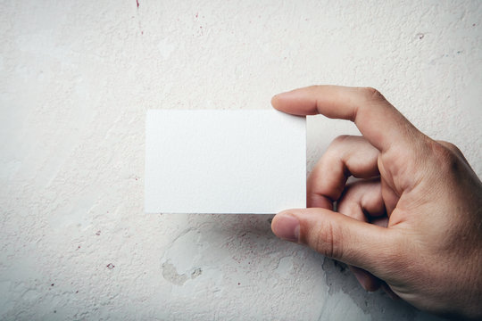 Closeup of male hand holding white business card on concrete wal