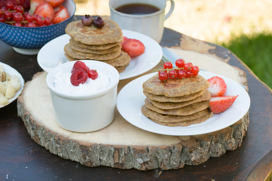 Breakfast in the garden: paleo style grain free banana almond pancakes, coconut yogurt with berries, selective focus on redcurrants