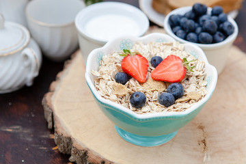 Breakfast in the garden: oatmeal cereals with berries on the dark wooden table, selective focus