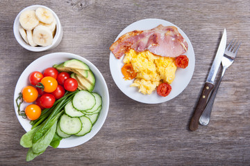 Breakfast: scrambled egg and bacon with salads, vegetables on a dark wooden table, selective focus