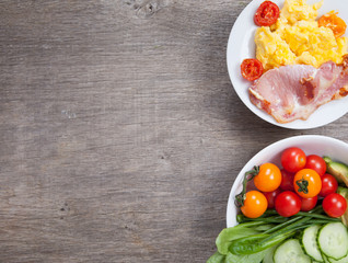 Breakfast: scrambled egg and bacon with salads, vegetables and banana on a dark wooden table, selective focus