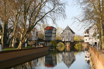 River in small German town with bridge and a house on bridge and reflections in water.