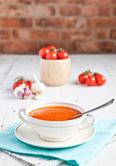 Tomato soup with tomatoes on the background on the white table, brick wall background