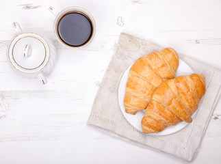 Two croissants with coffee on the white table, view from above