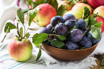 Ripe apple and plums in ceramic bowl