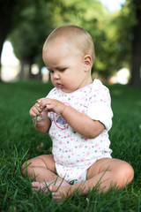 Happy baby with light and fluffy hair sitting on the grass