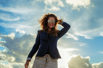 Obraz premium Smiling redhead girl posing over blue sky with clouds.