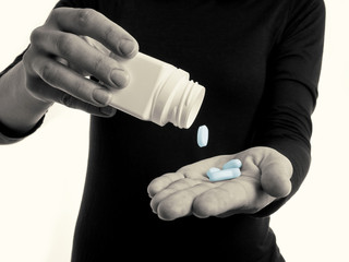 Black and white toned photo with blue  pills falling on the female hand