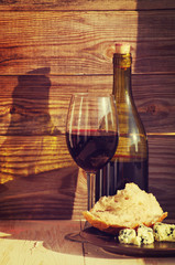 Bottle of red wine, glass with wine, cheese and white loaf on a wooden background
