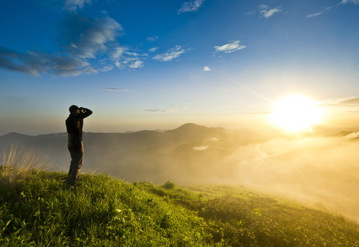 man on a hill at sunset with camera making photo