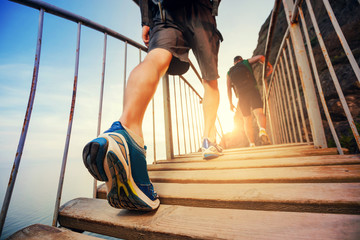 Men hiking in mountains, walking on wooden bridge at sunset. Healthy lifestyle.