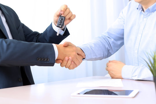 Car salesman handing over the keys for a new car to a young busi