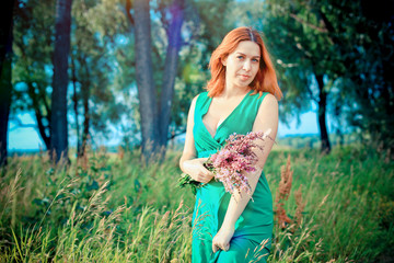 Romantic red-haired young woman in green long dress Walking