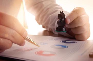 Closeup of businessman working with document graph and holding a chess piece.