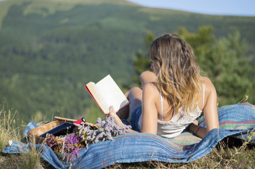 Young woman laying on a blanket and reading a book on a picnic i