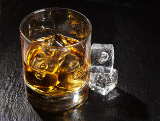 Glass of whiskey with ice on black stone table