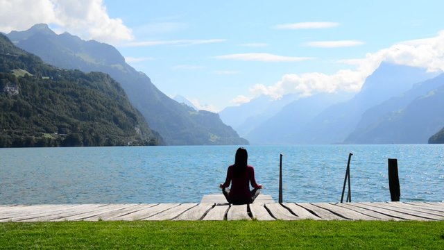 Woman sitting in lotus position and meditating on the lake. The breeze shakes her long hair.