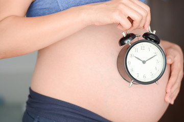 Pregnant woman holding clock suggesting time to arrive