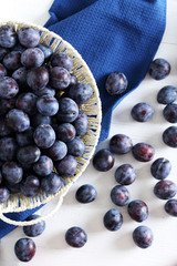 Fresh plums in basket on the white wooden background