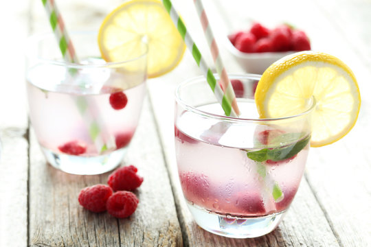 Raspberries and juice in glass on grey wooden background