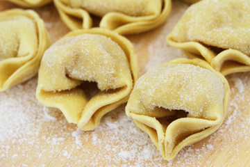 Uncooked tortellini on wooden board, closeup
