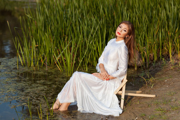 Beautiful girl sits on shore of the lake.
