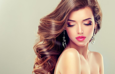 Beautiful model brunette with long curled hair and jewelry earrings 
