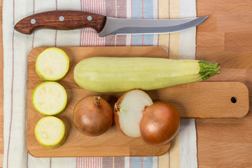 Vegetable marrow and onions lie on a cutting board next to a kni