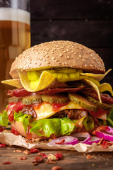Delicious beef burger with nachos and beer on wooden table.