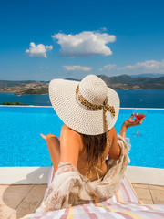 Woman holding a fresh cocktail relaxing by the infinity swimming