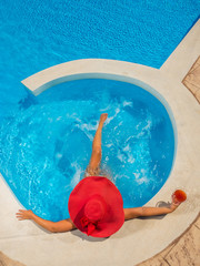 Woman in hat relaxing at the pool with cocktail