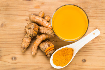 Healthy turmeric roots drinks in a transparent glass on wooden surface