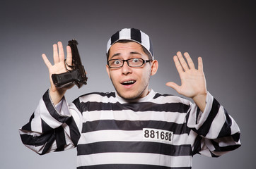 Young prisoner with handgun against gray