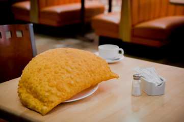 Large empanada and white coffee cup sitting on restaurant table