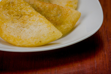 Closeup three perfect empanadas on white plate with wooden