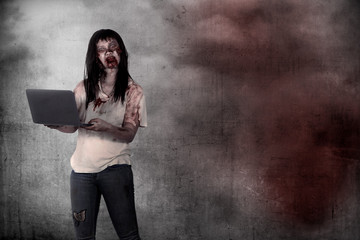 Female zombie holding laptop over grunge background