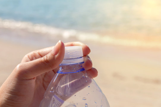 Pet bottle with water on the sea with hand closeing plug on beac