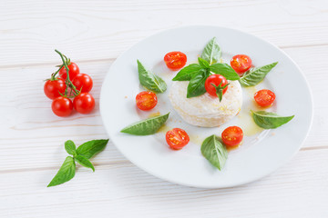 a round piece of cheese with basil and cherry tomatoes on a white plate