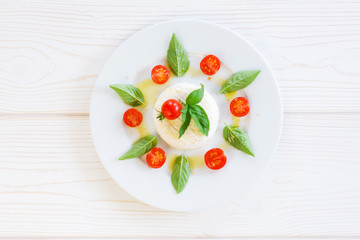 round piece of cheese with basil and cherry tomatoes on a white plate
