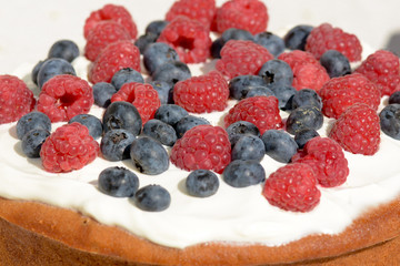 Cake with frosting covered in raspberries and blueberries