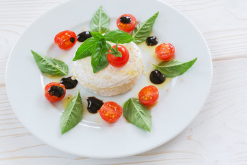 round piece of cheese with basil and cherry tomatoes on a white plate