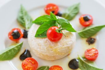 round piece of cheese with basil and cherry tomatoes on a white plate