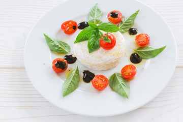 round piece of cheese with basil and cherry tomatoes on a white plate
