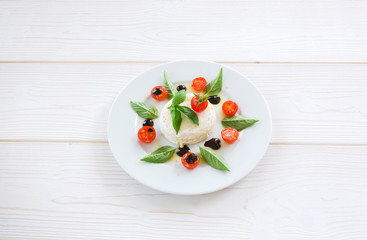 round piece of cheese with basil and cherry tomatoes on a white plate