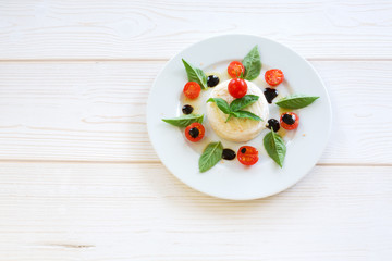 round piece of cheese with basil and cherry tomatoes on a white plate